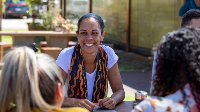 Close-up of young aboriginal people sitting around a table together outdoors in the sun in Australia.