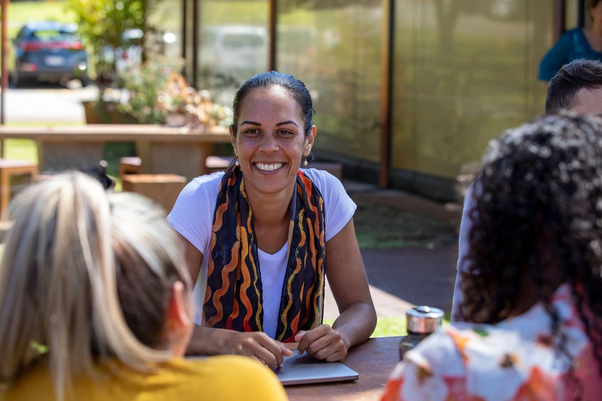 Close-up of young aboriginal people sitting around a table together outdoors in the sun in Australia.